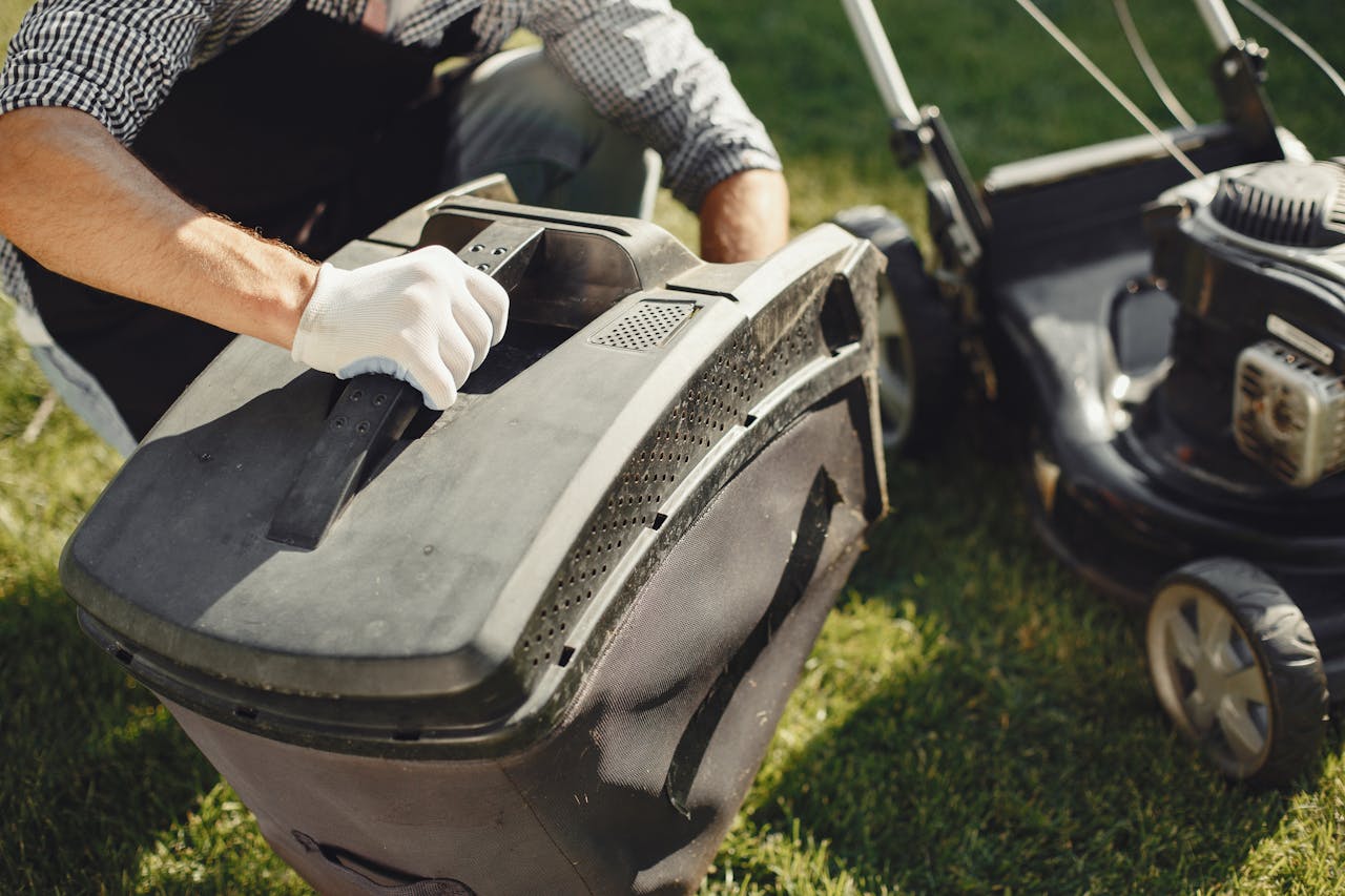An adult man replacing a lawn mower bag on a sunny day in the yard.